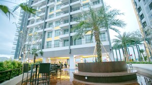A modern multi-story building with balconies, a central courtyard with a palm tree, and outdoor seating areas. - H2H Maison De Luxe (Ipoh)