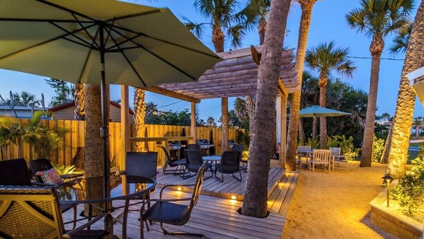 Un espace extérieur aménagé en terrasse, avec un sol en bois, du mobilier de jardin et des palmiers.