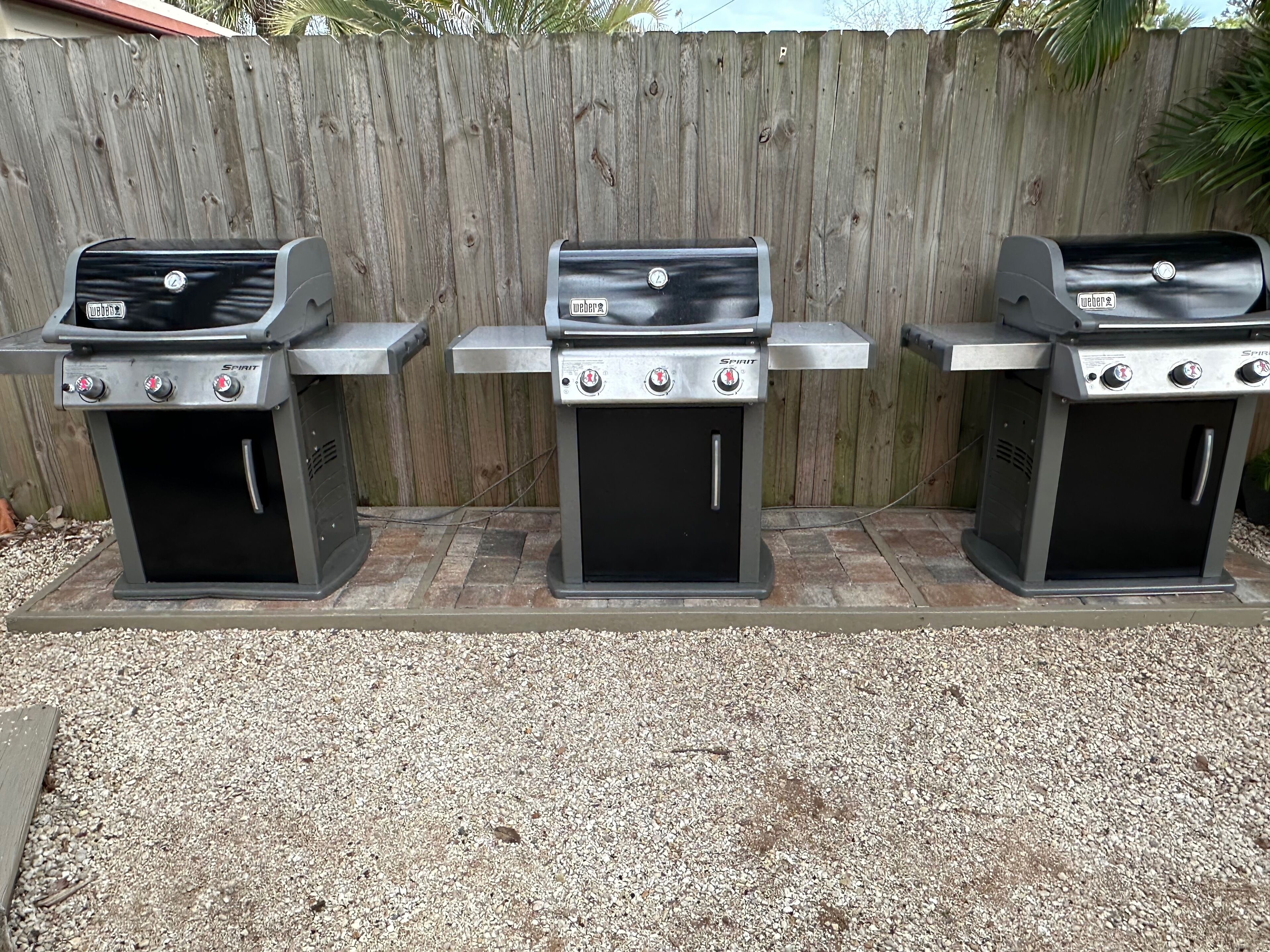 Tres parrillas Weber Spirit alineadas frente a una cerca de madera.