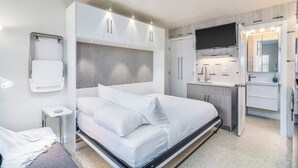 Une chambre d’hôtel moderne dotée d’un grand lit, d’une armoire intégrée, d’une télévision et d’une salle de bain avec un miroir et un lavabo.