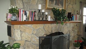 Lareira de pedra com prateleira que exibe livros, velas e um vaso com flores.