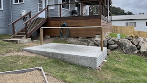 A residential deck with a wooden staircase leading to a covered area, a concrete platform, and a garden with a wooden border.