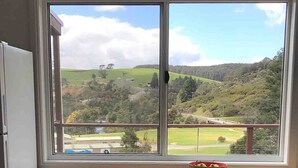A window with a view of a green landscape, a bowl on the windowsill, and a white door to the left.