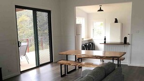 A modern living room with a large wooden table and a grey sofa. There is a sliding glass door leading to a balcony.