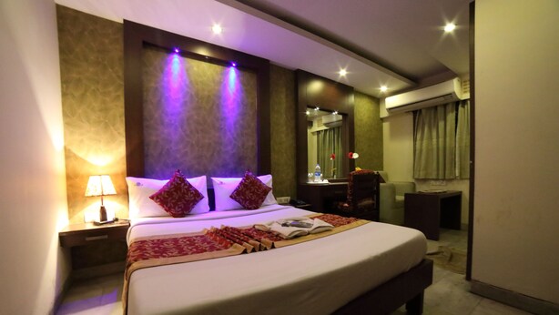 A well-lit hotel room with a large bed, a bedside table with a lamp, a mirror, and an air conditioning unit. - Bhimaas Temple Tree (Chennai)