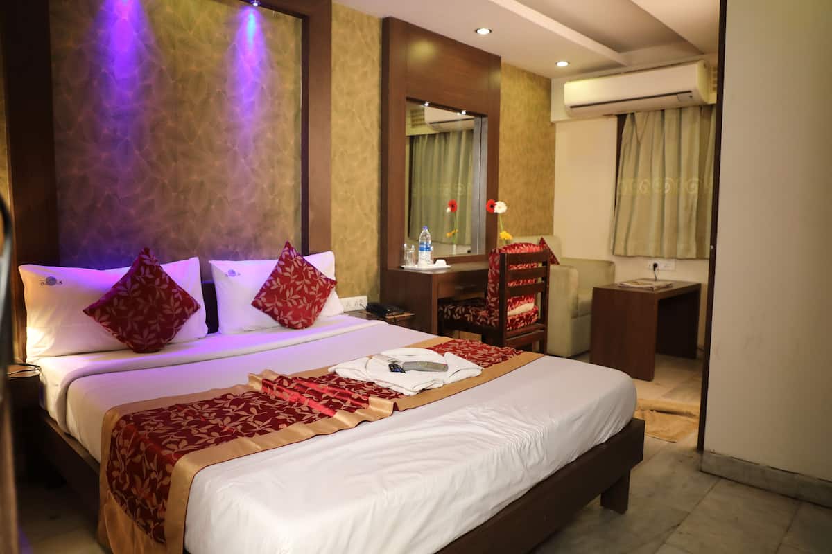 A hotel room with a large bed, a desk, a chair, and an air conditioning unit.
