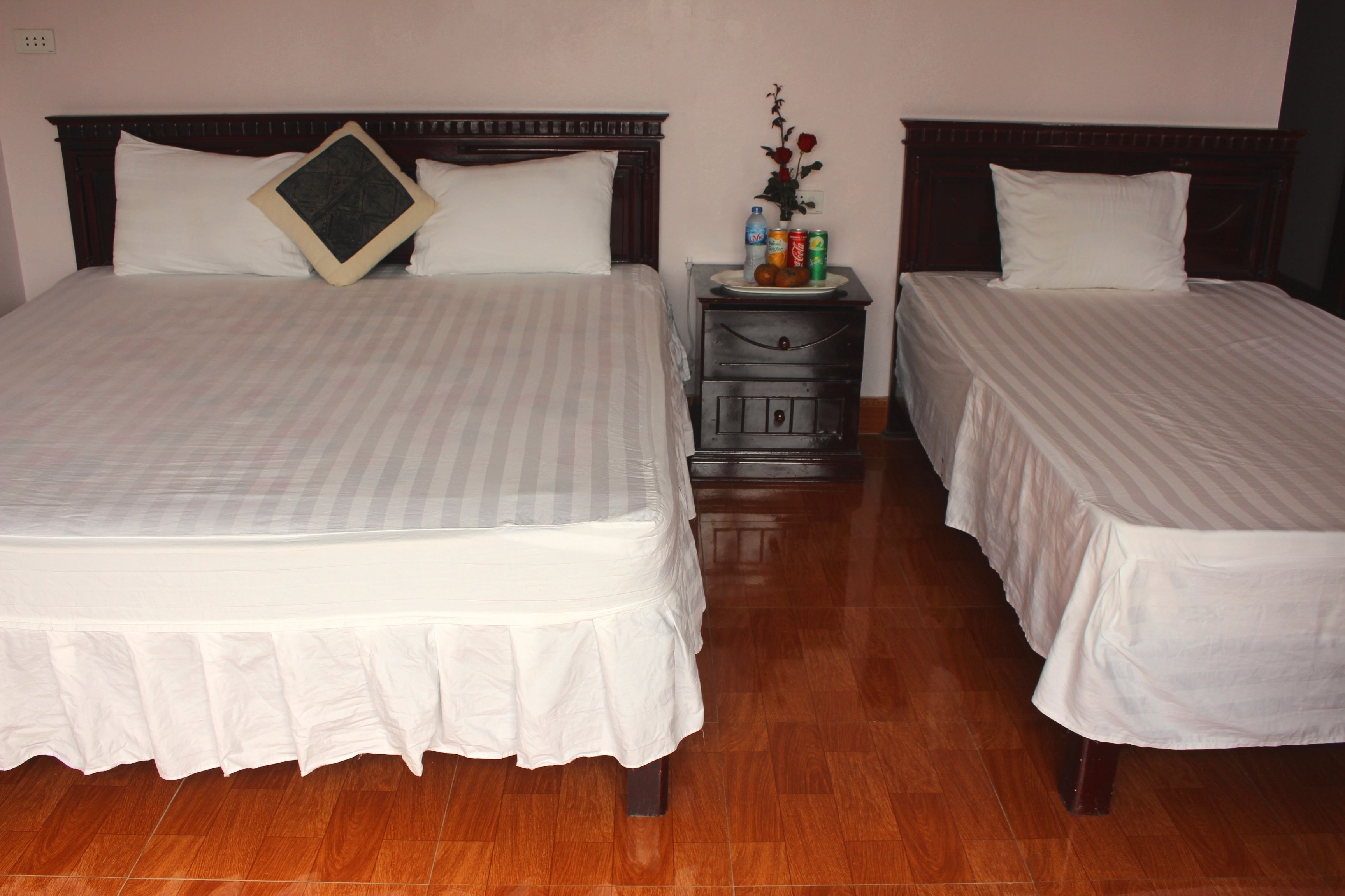 A hotel room with two beds, a nightstand with a vase of flowers, and a wooden floor.