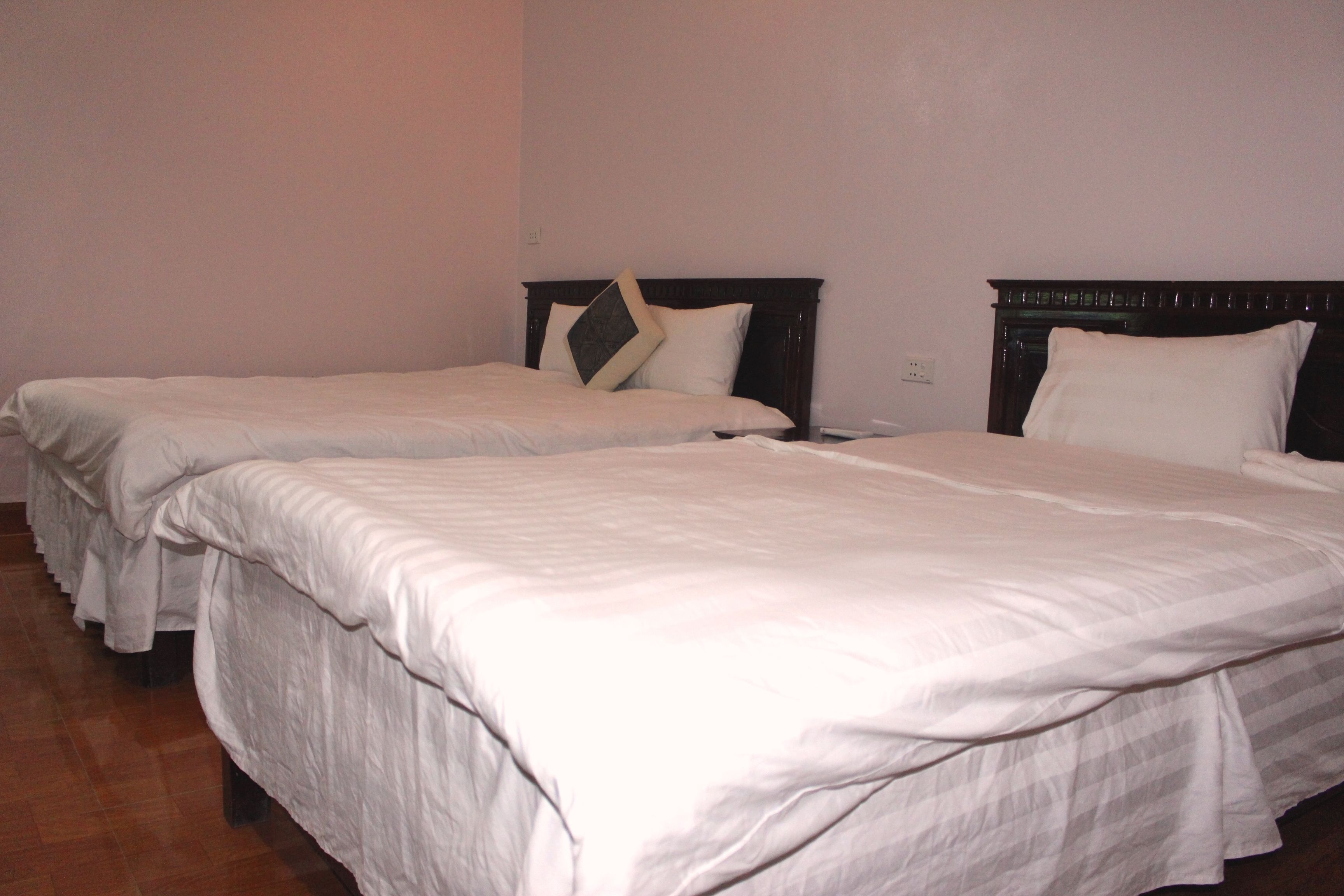 A hotel room with two single beds, each with a wooden headboard and white bedding.