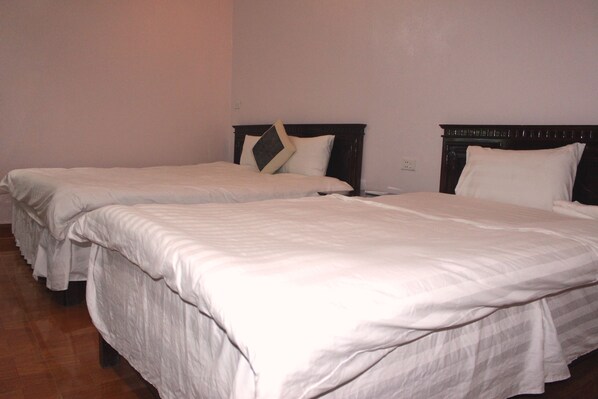Una habitación de hotel con dos camas individuales, cada una con cabecero de madera y ropa de cama blanca.