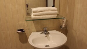 Een badkamer met een wastafel, een glazen plank waarop een opgevouwen witte handdoek ligt, en een klein plankje met toiletartikelen.