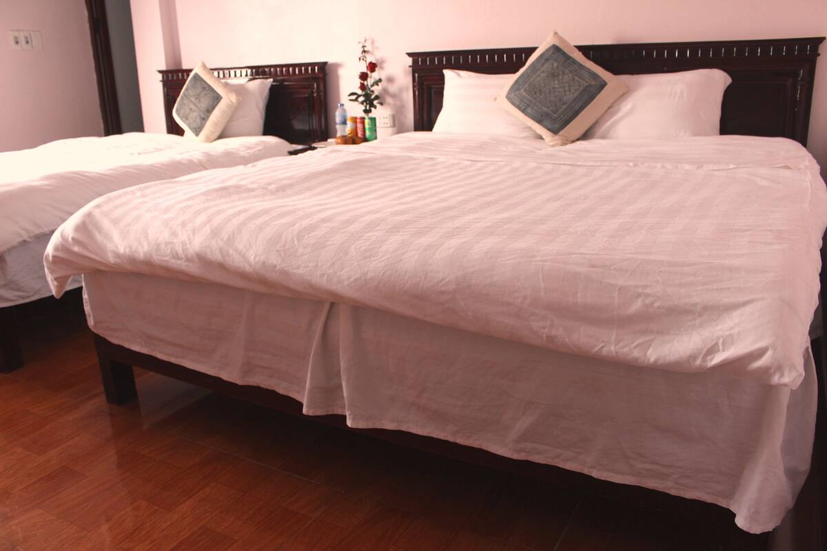 A hotel room with two single beds, wooden headboards, white linens, and a wooden floor.