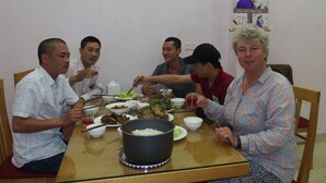 Een groep mensen dineert aan een houten tafel met verschillende gerechten en een rijstpot.