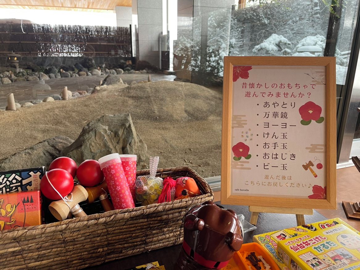 A table with a framed menu, a basket of items, and a view of a snowy landscape through a window.