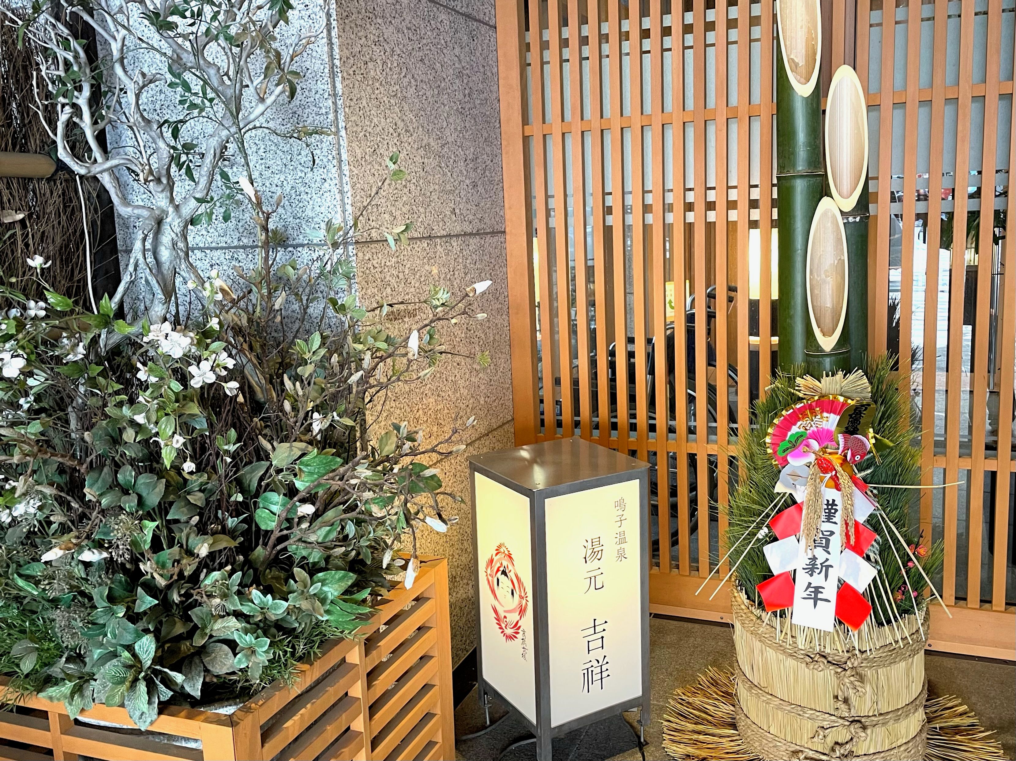 A traditional Japanese room with a wooden sliding door, a small table with a sign, and a decorative plant arrangement.