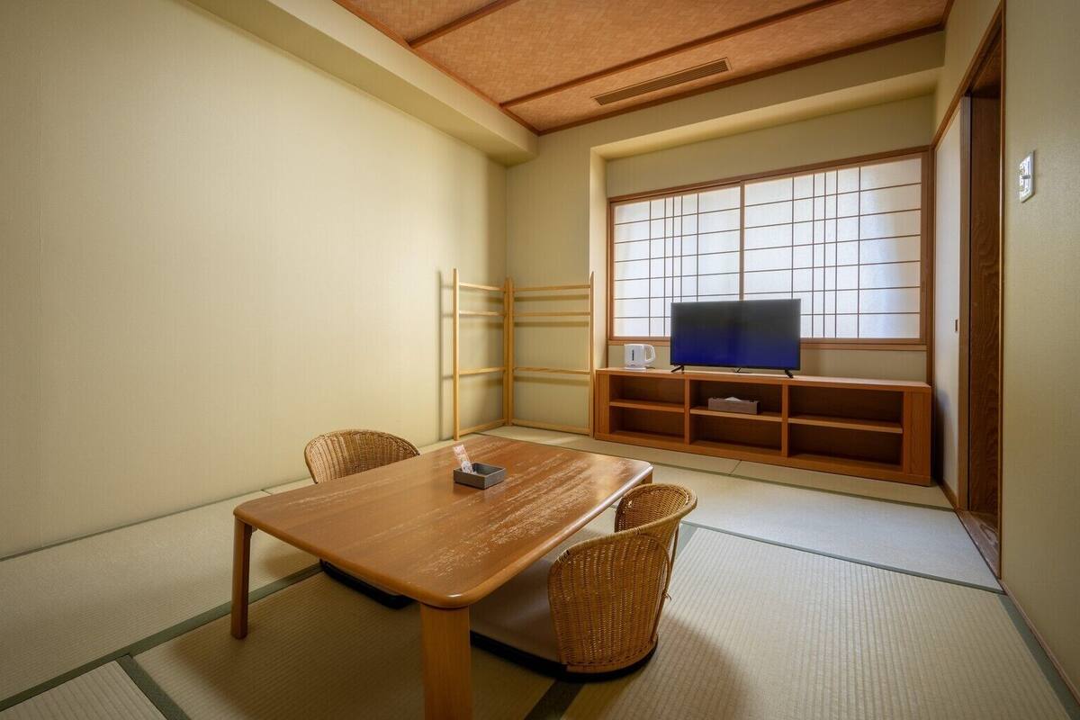 A traditional Japanese room with tatami flooring, a low table, and a television on a wooden stand.