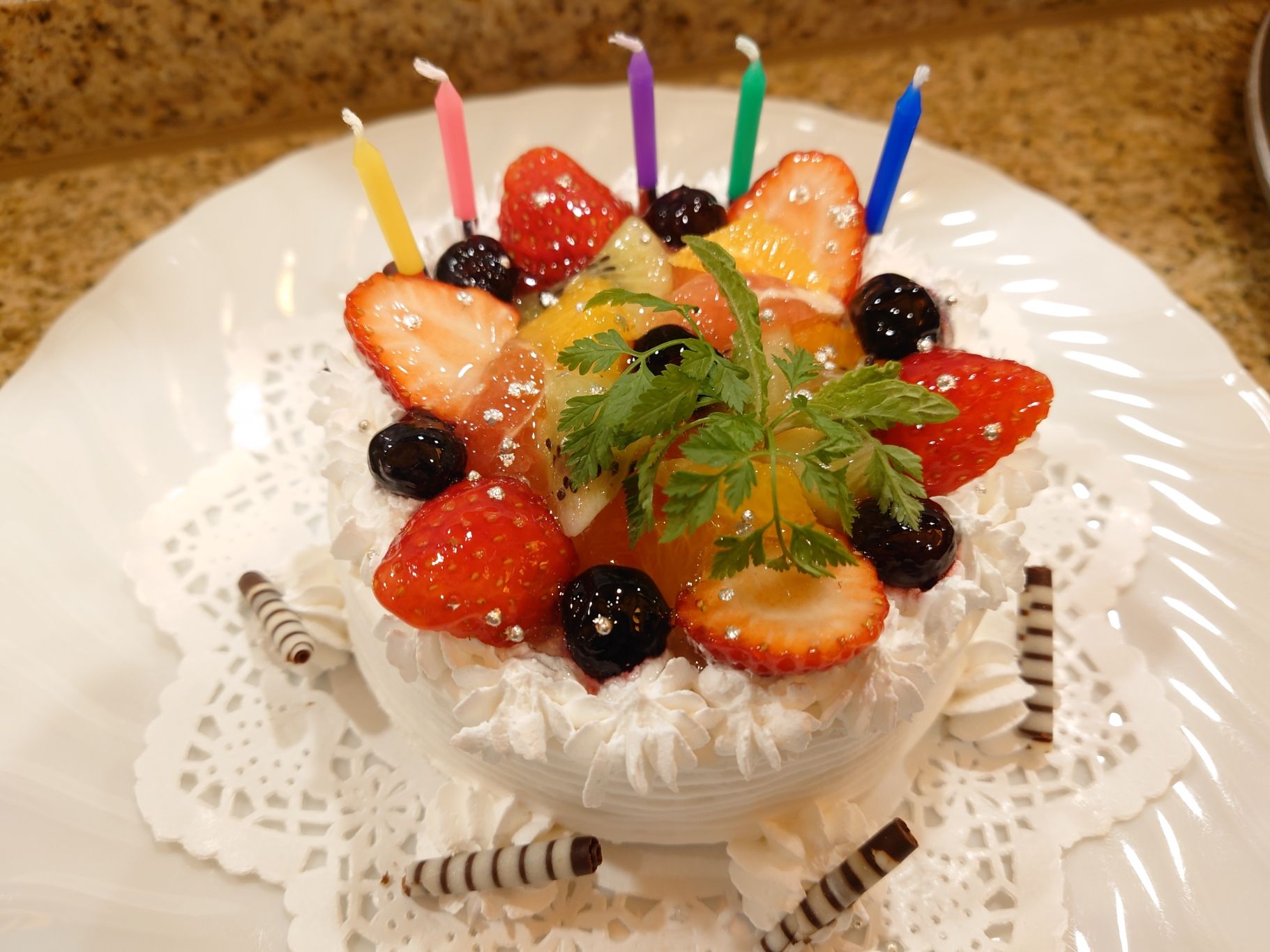 A dessert with strawberries, blackberries, and a sprig of parsley on a white plate with a lace doily underneath.