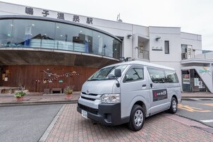 Una camioneta blanca estacionada frente a un edificio con fachada de vidrio curvo y pared de madera con decoraciones coloridas.
