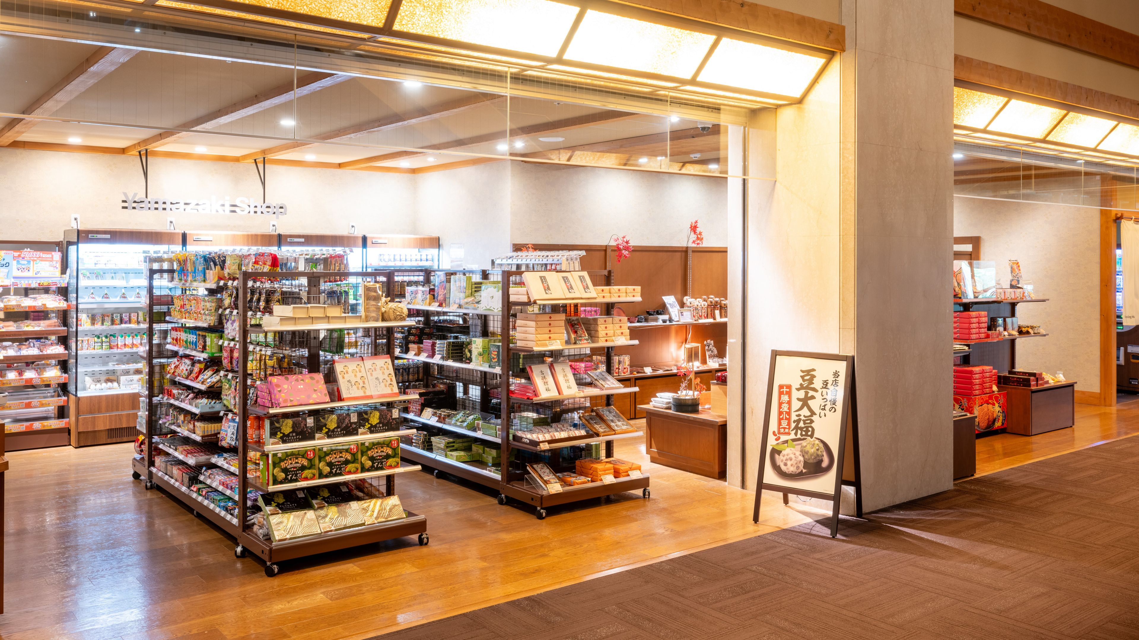 A well-lit store with various shelves stocked with products, a refrigerated display, and a wooden floor.