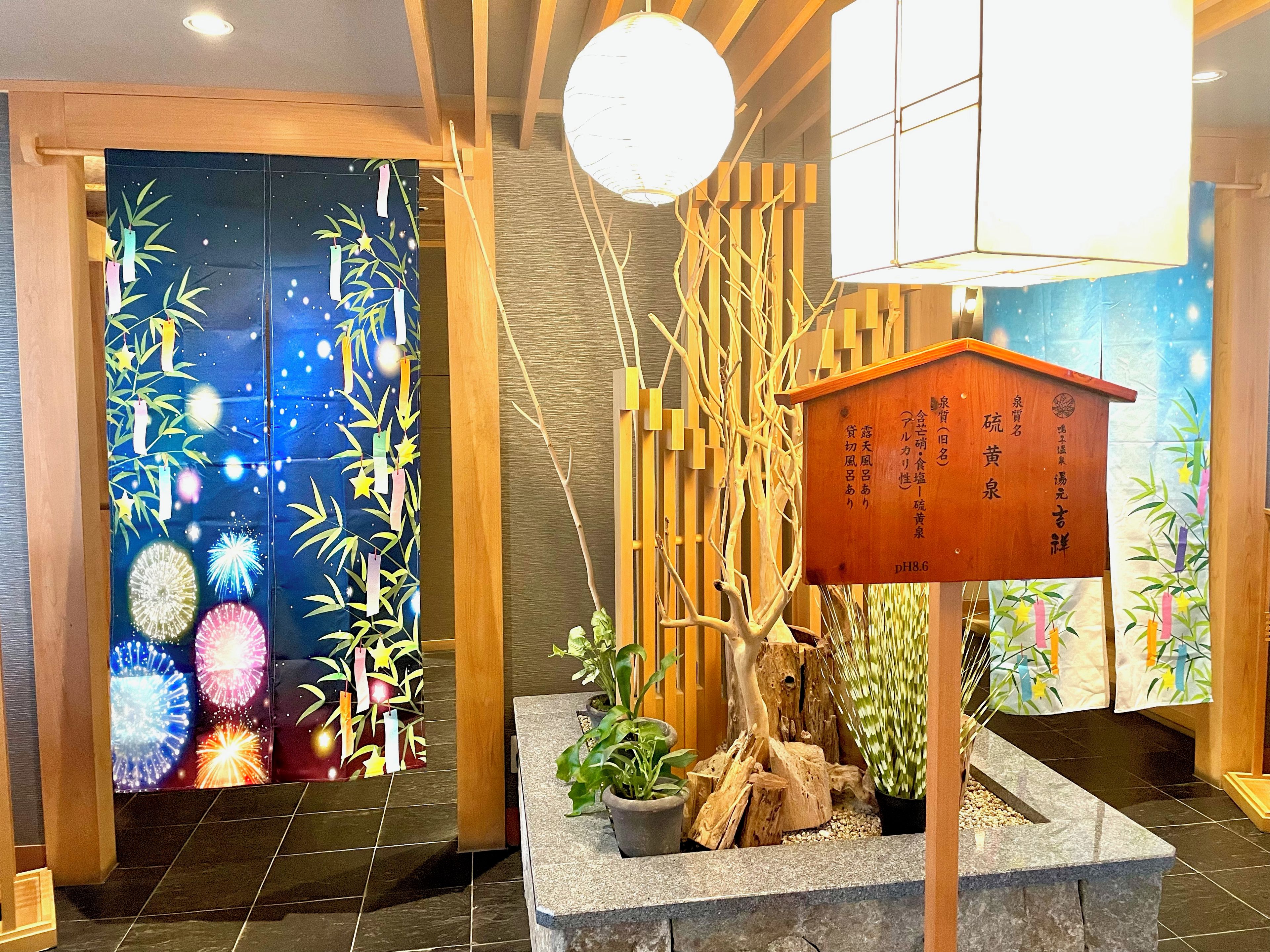 A reception area with a traditional Japanese aesthetic, including a wooden reception desk, a decorative wall with bamboo motifs, and a potted plant.