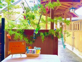 Una pérgola de madera con una cesta tejida que contiene material de papelería, un letrero con texto japonés y una planta de bambú.