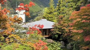 A traditional Japanese house with a sloped roof, surrounded by lush greenery and a small pond.