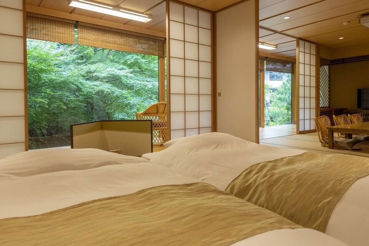 A traditional Japanese-style room with tatami flooring, a low table with chairs, and a large window overlooking greenery.