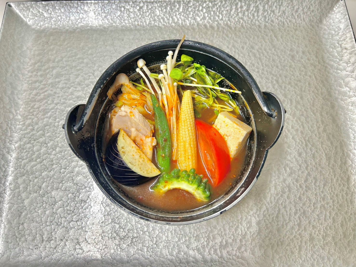 Eine Schüssel Suppe mit verschiedenen Gemüsesorten und Tofu auf einer strukturierten Oberfläche.