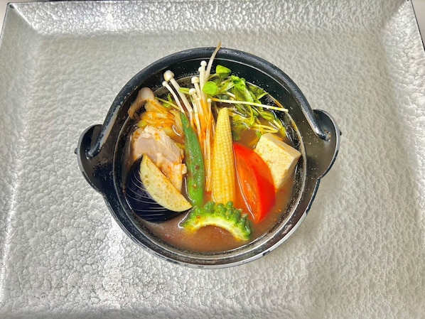 A bowl of soup with various vegetables and tofu on a textured surface.