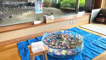 A room with a large window overlooking a rock garden, a blue mat with toys, and a small wooden stool with towels.