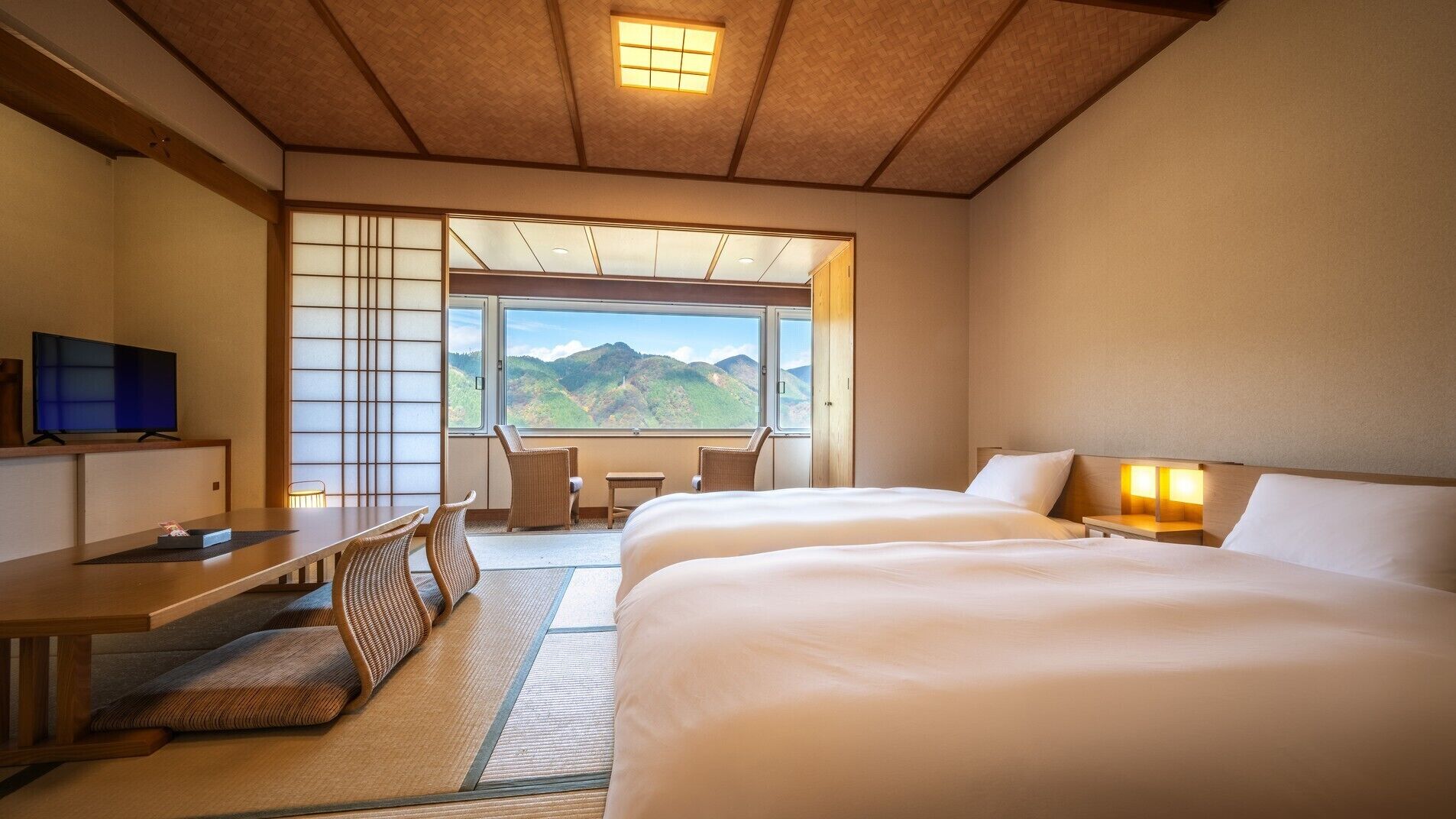 Habitación de hotel con cama, escritorio, silla, televisor y vistas a las montañas.