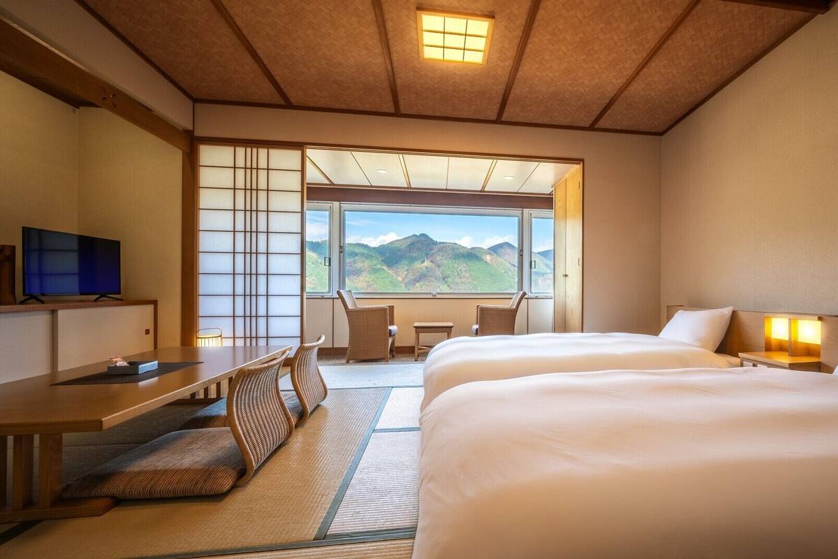 A hotel room with a bed, a desk, a chair, a TV, and a view of mountains.