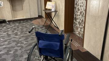 A wheelchair in a hotel hallway with a patterned carpet, a small table with a sign, and a door with a patterned wall.