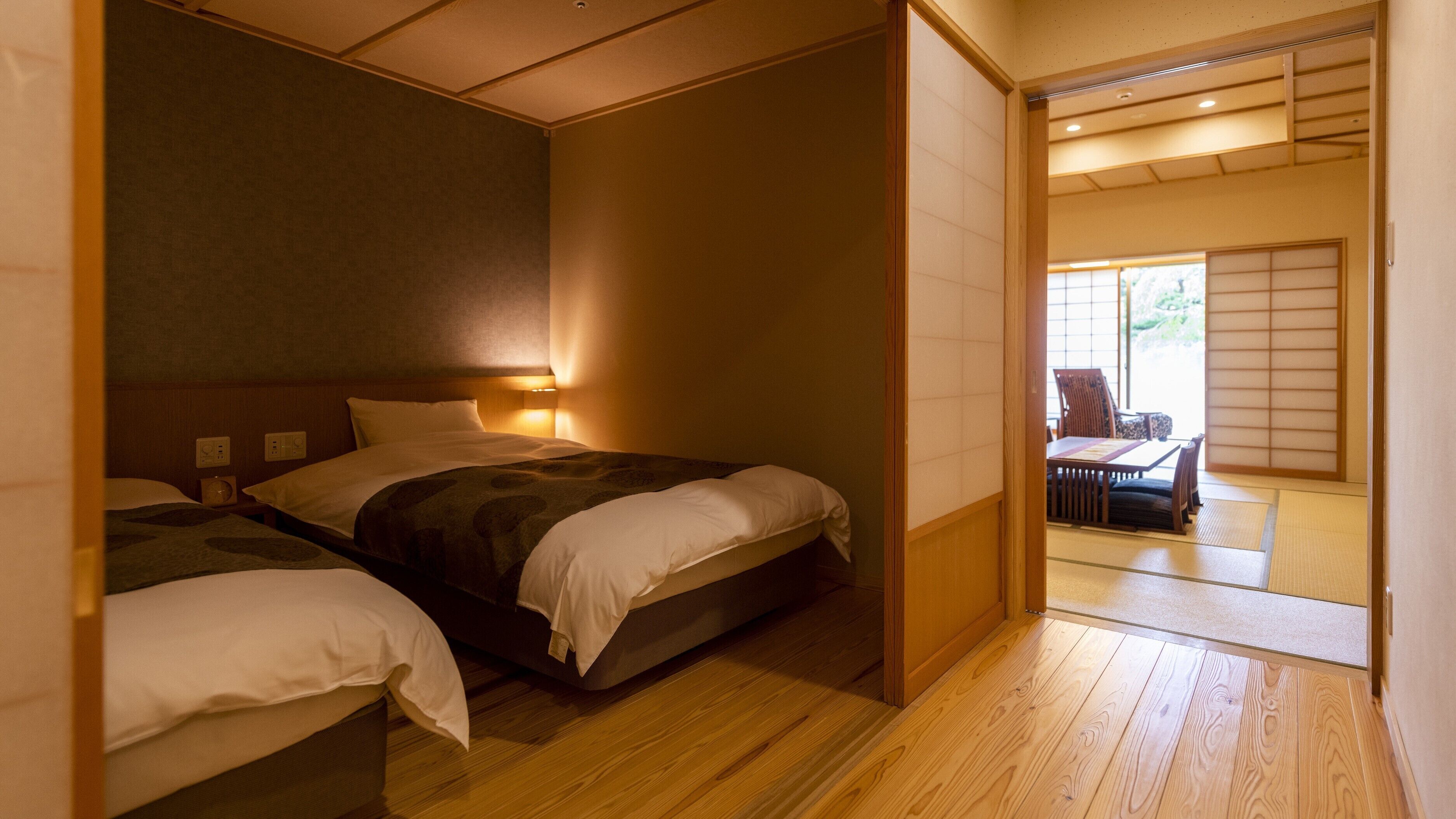 Un dormitorio de estilo japonés tradicional con dos camas, piso de madera y puertas correderas que dan a un comedor.