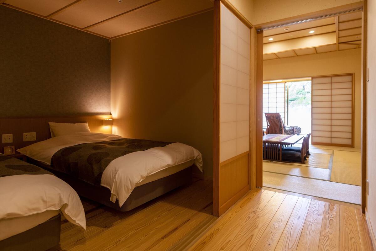 A traditional Japanese-style bedroom with two beds, a wooden floor, and sliding doors leading to a dining area.