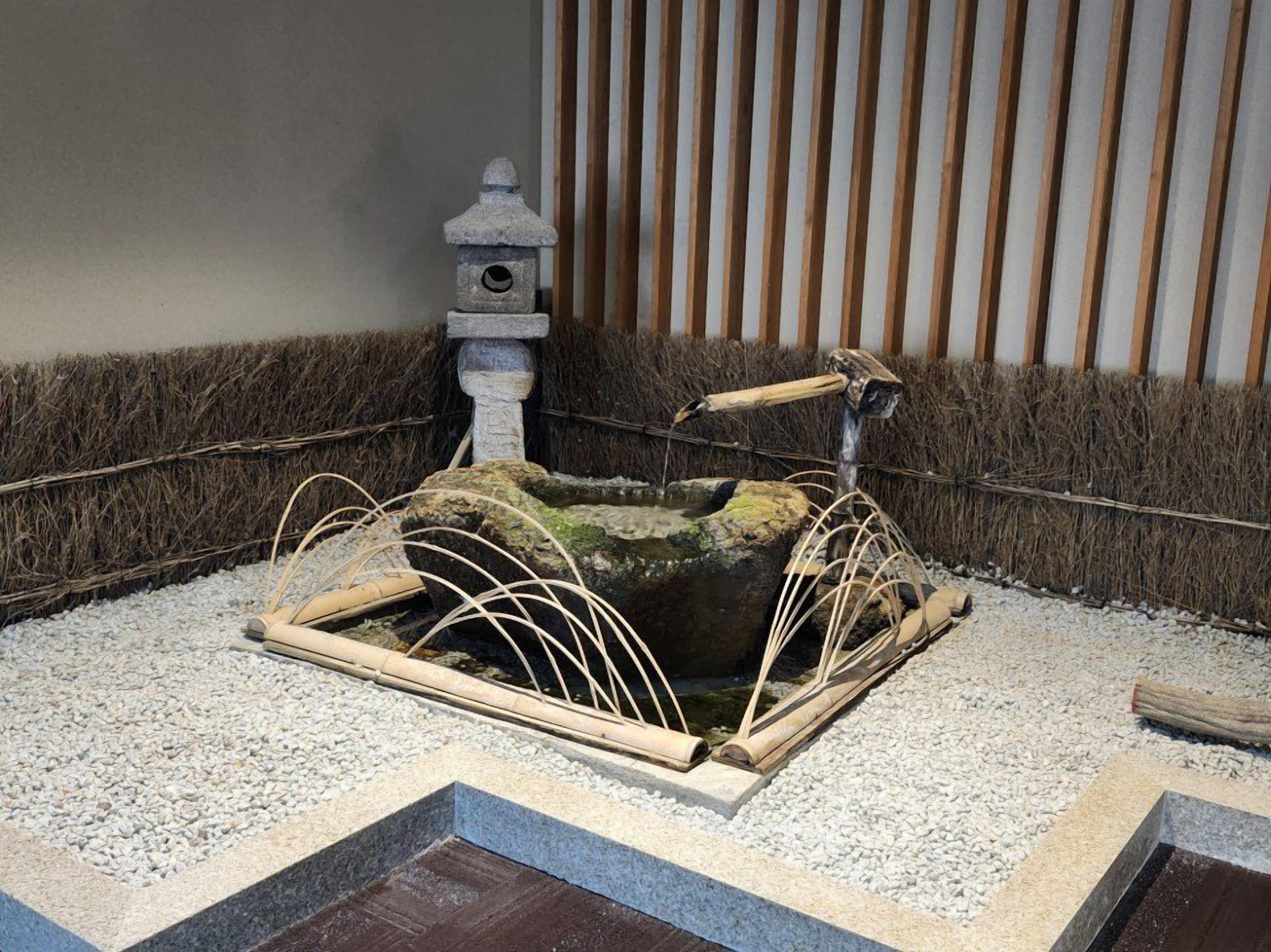 A traditional Japanese garden with a stone lantern, a small pond, and bamboo structures.