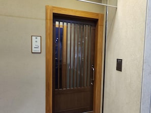 Una puerta de madera con un patrón a rayas verticales, un letrero con caracteres japoneses y una pequeña placa negra en la pared.