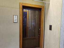Una puerta de madera con un patrón a rayas verticales, un letrero con caracteres japoneses y una pequeña placa negra en la pared.