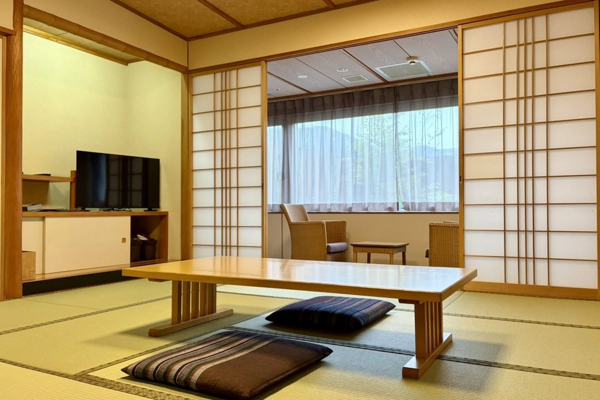 Una habitación japonesa tradicional con suelo de tatami, una mesa baja, cojines y puertas correderas.