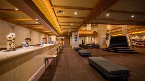 A hotel lobby with a reception desk, seating area, and a staircase.