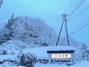 A snow-covered sign with Chinese characters, surrounded by trees and power lines.