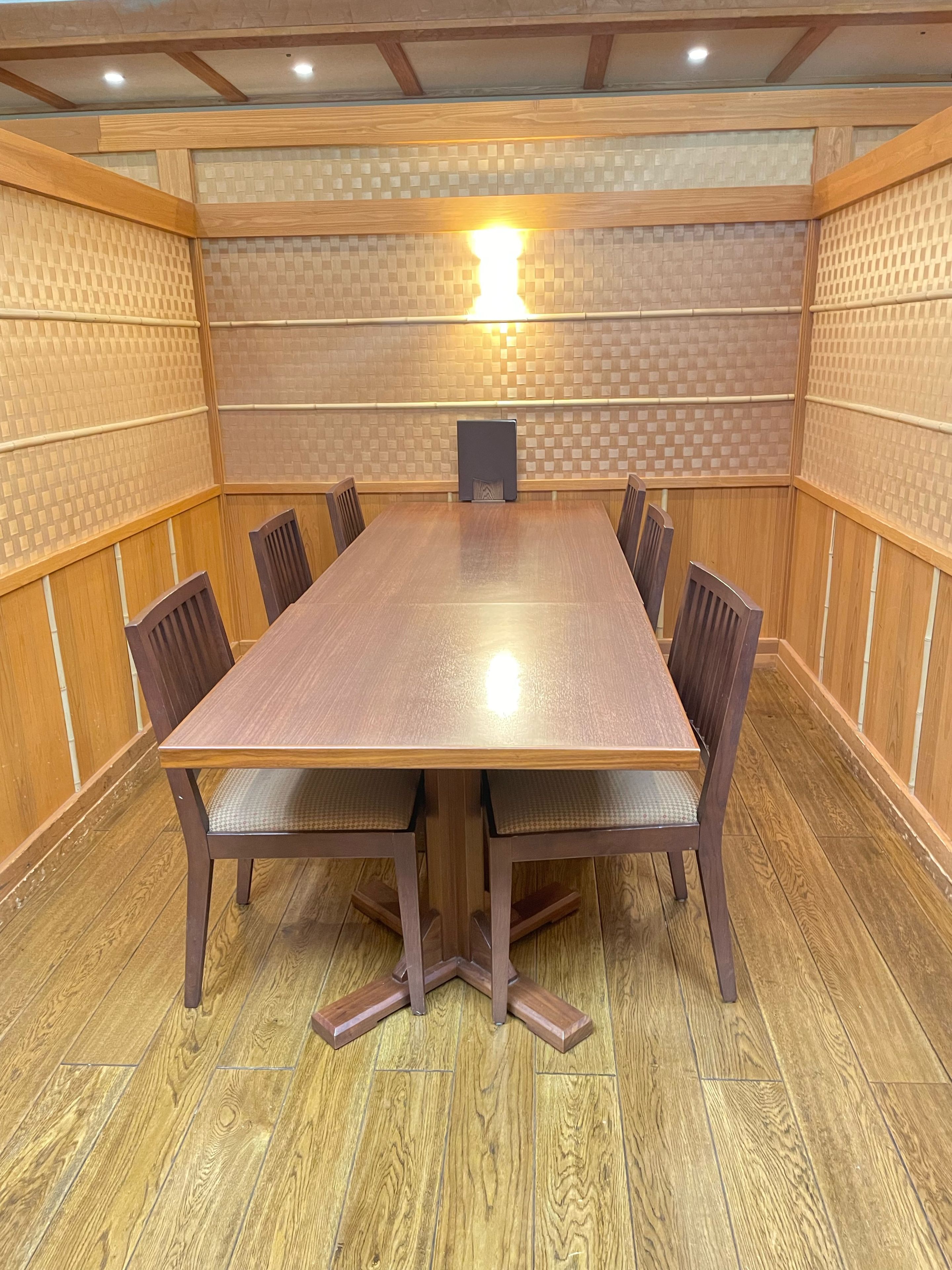 A conference room with a wooden table and chairs, a patterned wall, and a ceiling light.