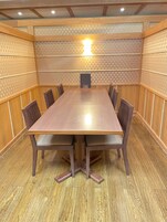 Un salón de conferencias con una mesa y sillas de madera, un papel tapiz decorativo y una lámpara en el techo.