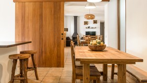 A wooden dining table with chairs, a basket of fruit, and a hanging light fixture in a room with a wooden door and tiled floor. - Villa Dalt S'Era - Free week from July 13 to 20 (Santa Eulària des Riu)