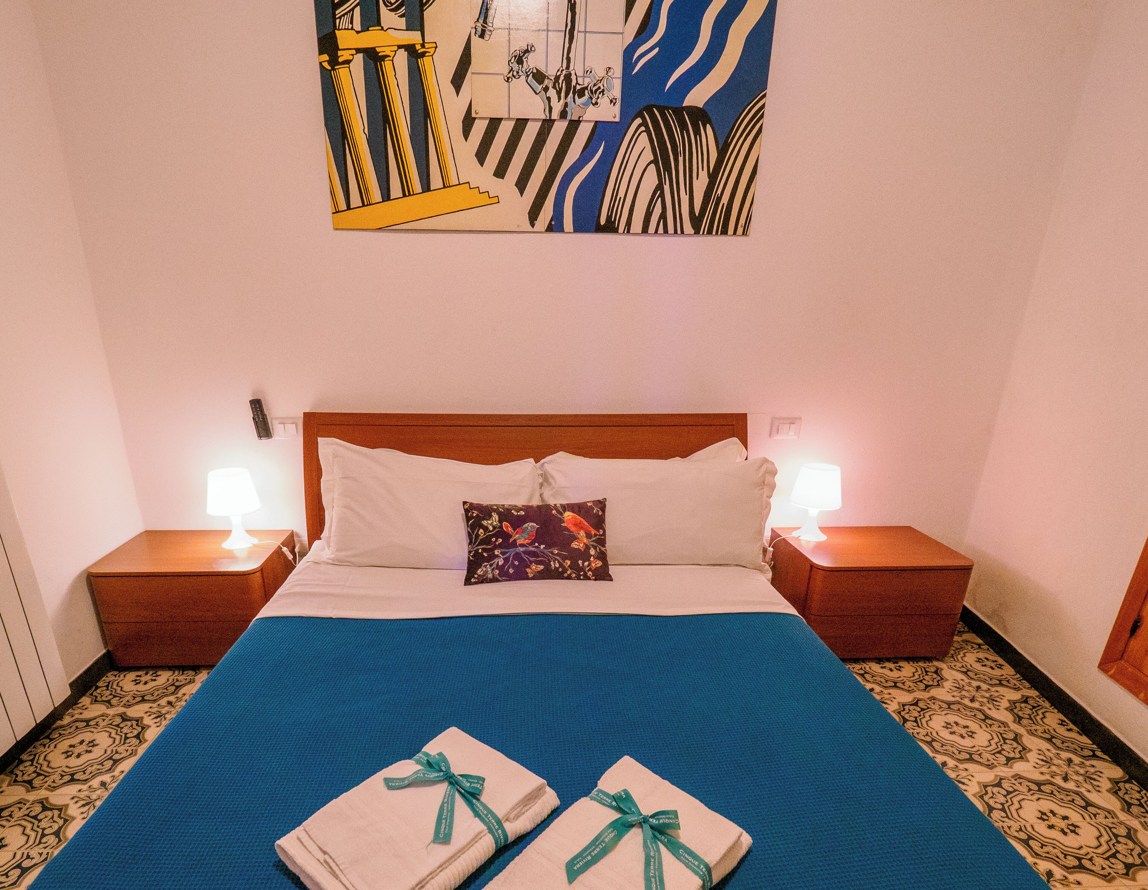 A hotel room with a large bed, two bedside lamps, a decorative pillow, and a painting on the wall.