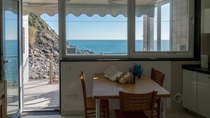 A dining area with a view of the sea and rocky terrain through large windows. - Unda de Ma Apartment with AC & Sea View Balcony (Vernazza)