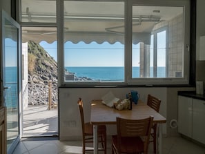 Uma área de refeições com vista para o mar e terreno rochoso através de grandes janelas.