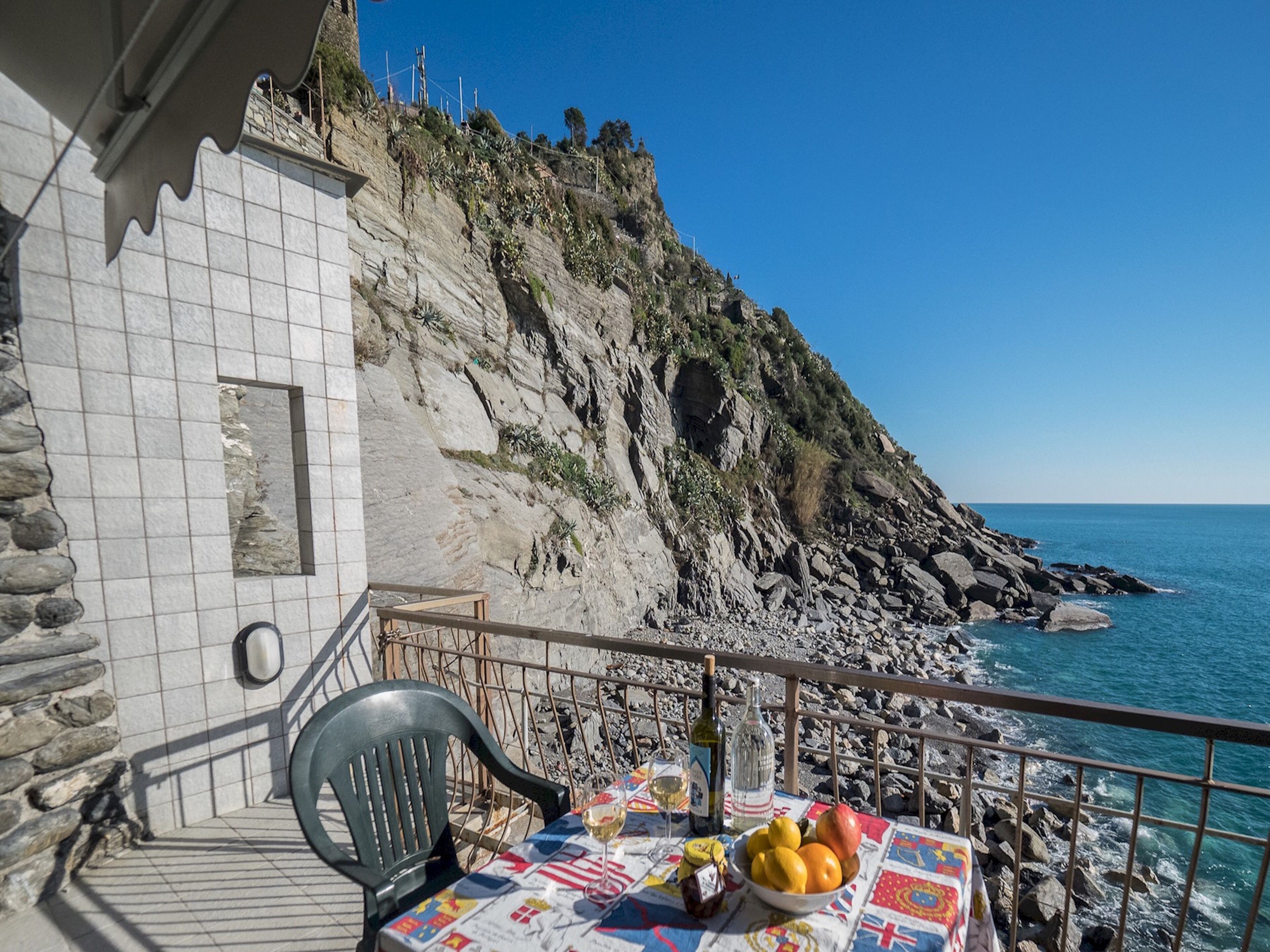 Un balcón con mesa lista para comer, con vista a un litoral rocoso y al mar.