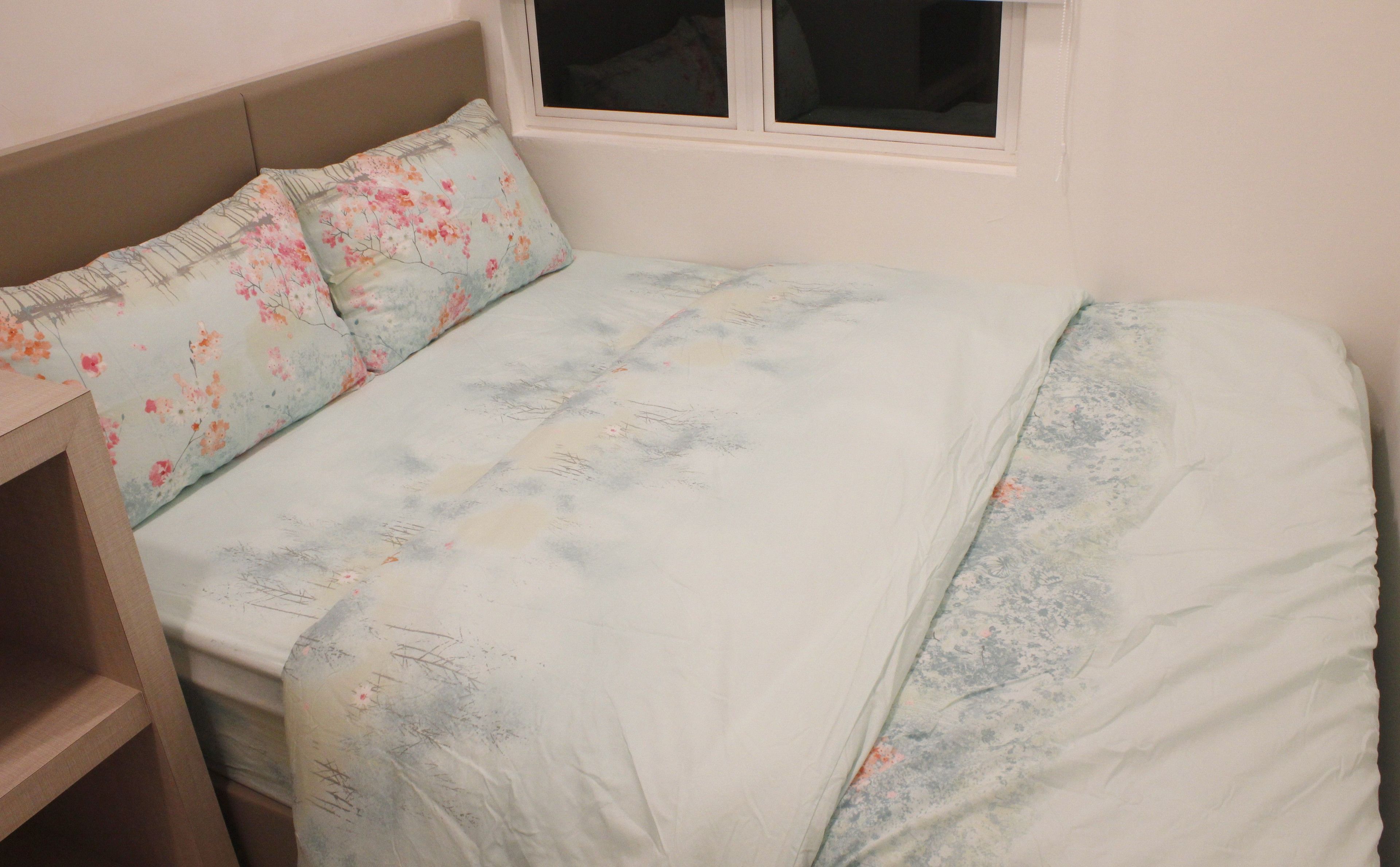 A neatly made bed with floral-patterned pillows and a light-colored bedspread.