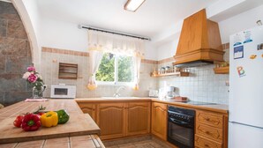 A kitchen with wooden cabinets, a built-in oven, and a window with curtains. - Villa Garlanda - PlusHolidays (Benissa)