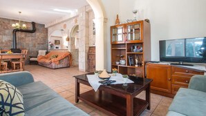 A living room with a stone wall, wooden furniture, a television, and a dining area with a table and chairs. - Villa Garlanda - PlusHolidays (Benissa)